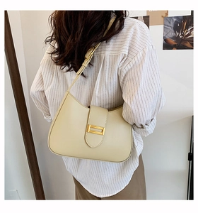 Close-up of cream-white crescent baguette bag with golden buckle and adjustable strap