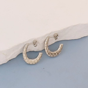 Detailed macro view of silver C-shape earrings with textured honeycomb pattern on white stone