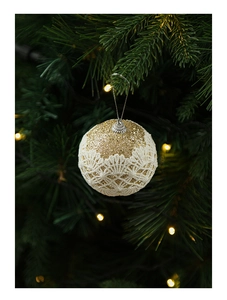 Close-up of golden glitter Christmas ball with white lace hanging on a festive tree