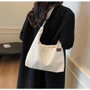 Close-up of white canvas tote bag with brown leather label worn by model in black suit