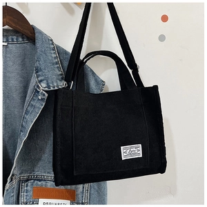 Close-up of black corduroy tote bag featuring a white textile brand label on the front