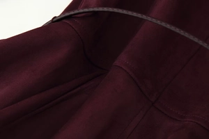 Macro detail of burgundy suede jacket showing fine stitching and leather trim texture