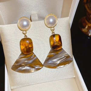 Close-up of vintage resin fan earrings with pearl studs on beige satin display