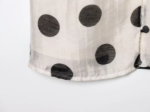 Detail of white polka dot top showing sheer fabric texture and button placket