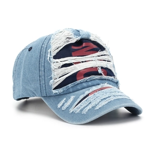 Detailed close-up of distressed blue denim baseball cap with frayed holes and red embroidery