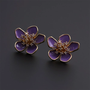 Dettaglio di orecchini a fiore placcati in oro con smalto viola e centri in cristallo lucente