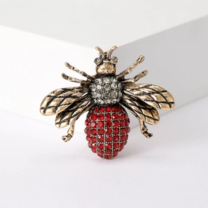 Detail of vintage gold bee brooch with red and clear rhinestones on white background