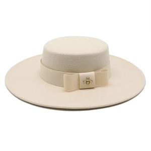 Detailed view of beige wool boater hat featuring a ribbon bow and golden bee accessory