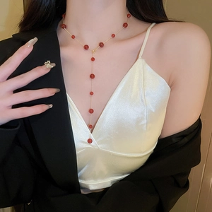 Detail view of long Y-shaped gold plated necklace with red beads on a fashion model