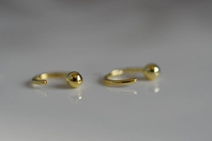 Vista macro de pendientes de aro dorados en forma de C con detalle de bola de metal