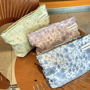 Floral jacquard travel makeup bags in green, pink, and blue colors on a chair