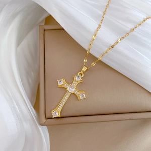 Close-up of golden cross necklace with inlaid clear crystals on white silk background