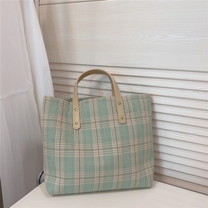 Detailed view of green plaid tote bag with faux leather handle and gold rivet reinforcement