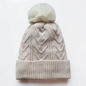 Beige knit winter beanie for women with faux fur pompom and pearl accents on white background