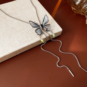 Detailed close-up of butterfly pendant necklace with tassels and blue-green wings