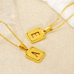 Detail of gold alphabet square pendants with matte texture and engraved letters E and A