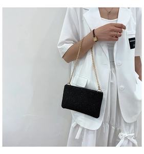 Detail of black rhinestone clutch bag with gold chain strap worn by model