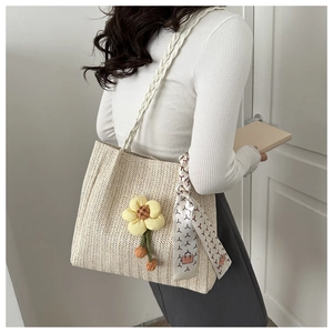Detail of woven straw tote bag featuring a yellow flower and patterned silk scarf handle