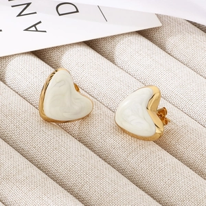 Detail of heart-shaped white enamel earrings with gold edges on beige fabric