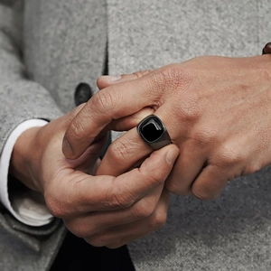 Close-up of a men's vintage black square resin signet ring on finger with a grey suit