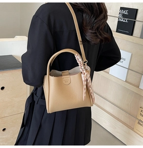 Detail of beige lychee pattern leather bucket bag with decorative plaid scarf handle