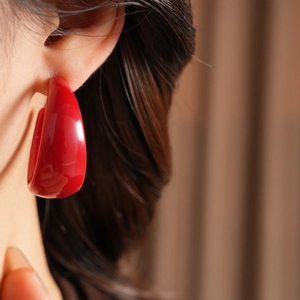 Close-up of a large glossy red resin C-shaped hoop earring worn on a model's ear