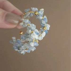 Detail of C-shaped hoop earrings with blue natural stones hand-wrapped on gold wire