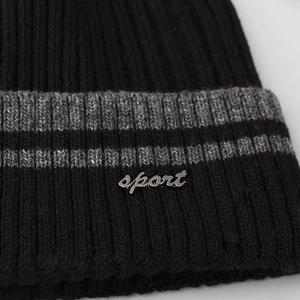 Close-up of black ribbed knit beanie with grey stripes and a silver sport metal badge