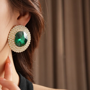 Detail view of large green emerald-cut crystal earrings with double rhinestone halo on a model