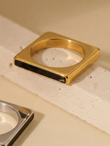 Detailed view of square 18k gold plated ring with black enamel inlay on stone surface