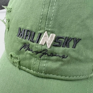 Macro detail of green baseball cap featuring distressed holes and MALINSKY embroidery