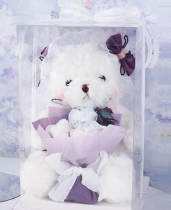Close-up of white plush teddy bear with purple soap roses in a transparent gift box