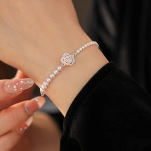 Macro detail of pearl bracelet with crystal-encrusted rose flower on wrist