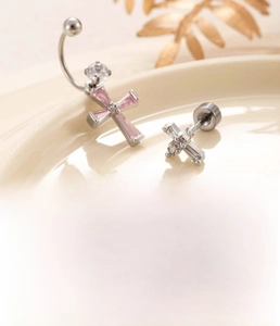 Detail of silver cross ear piercing studs with pink zircon and polished titanium steel