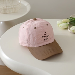 Detail of kids baseball cap featuring pink fabric and embroidered smiley face thank you text