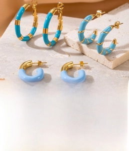 Detail of C-shaped stainless steel earrings with gold plating and blue enamel accents