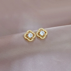 Macro shot of gold four-leaf clover earrings with zircon inlay on silk background
