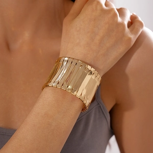 Detail view of a metallic gold geometric wide cuff bracelet worn by a model on the wrist