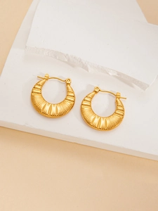 Close-up of golden hoop earrings with radiant texture on white stone surface