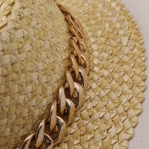 Gros plan sur la texture d'un chapeau de paille orné d'une grosse chaîne en métal doré