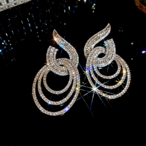 Close-up of silver geometric dangle earrings with shimmering crystals on black background