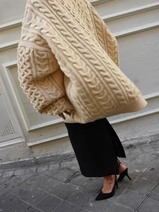 Pull beige oversize en maille torsadée à col roulé avec jupe noire et talons hauts