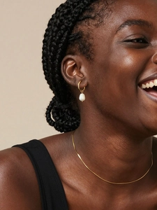 Detailed view of model wearing gold hoop earrings with white teardrop freshwater pearls