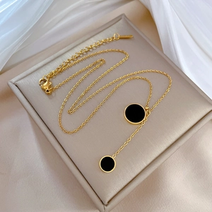 Golden titanium steel necklace with dual black disc pendants on a beige velvet display case