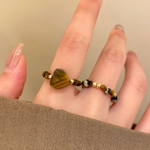 Macro shot of tiger eye stone heart beaded ring with golden metal beads on finger