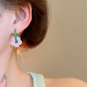Close-up of model wearing green glass hoop earrings with purple flower charms