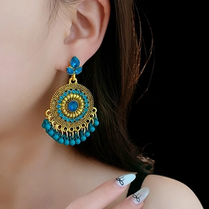 Close-up of vintage gold earrings with blue gemstones and hanging beaded tassels on model