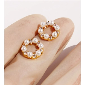 Mini pearl and zircon wreath stud earrings in gold finish held on a fingertip