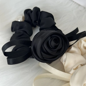 Close-up of black satin scrunchie featuring large rose flower and ribbon on white fur