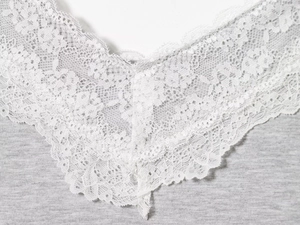 Detailansicht der weißen Spitze auf grauem Strickstoff mit V-Ausschnitt-Stickerei